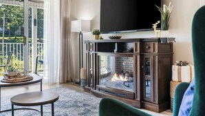 A living room with a fireplace, a television above it, and a view of the outdoors through a sliding glass door. - Vansen's Golfshores Inviting, Cozy Condo on Golf Course! (Branson)