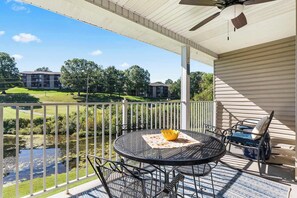 A covered outdoor area with a table and chairs, a view of a golf course, and a building in the background. - Vansen's Golfshores Inviting, Cozy Condo on Golf Course! (Branson)