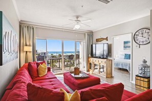 A spacious living room with a red sofa, a television, and a balcony with a view of the ocean.