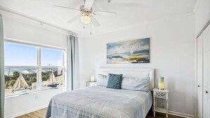 A bedroom with a bed, a ceiling fan, a painting, and a window with sailboats. - 🌊Beautiful Peek of the Gulf~Pools~Walk2Beach~On the Beach🌊 (Miramar Beach)