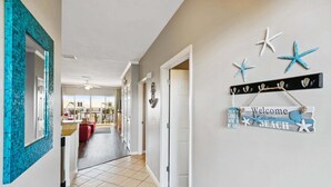 A hallway with a tiled floor, a mirror with a blue mosaic frame, a welcome sign with starfish and the word 'BEACH', and a coat rack. - 🌊Beautiful Peek of the Gulf~Pools~Walk2Beach~On the Beach🌊 (Miramar Beach)