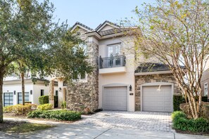 A two-story house with a stone facade, a balcony, and a garage. - Theater Room | Games Room |  Kids Themed Bedrooms | Private Pool with Golf Course Views (Kissimmee)
