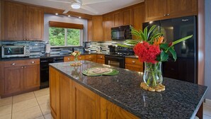 Eine moderne Küche mit Holzausstattung, Granit Arbeitsplatten, einer zentralen Kochinsel, einem Kühlschrank und einer Mikrowelle.