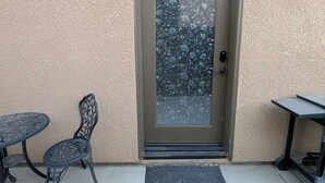 Una puerta con un panel de vidrio esmerilado, una pequeña mesa exterior, una silla y un felpudo.