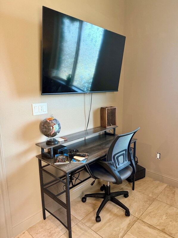 Un espace de travail aménagé à la maison, comprenant un bureau, une chaise, un téléviseur, un globe terrestre et un haut-parleur.