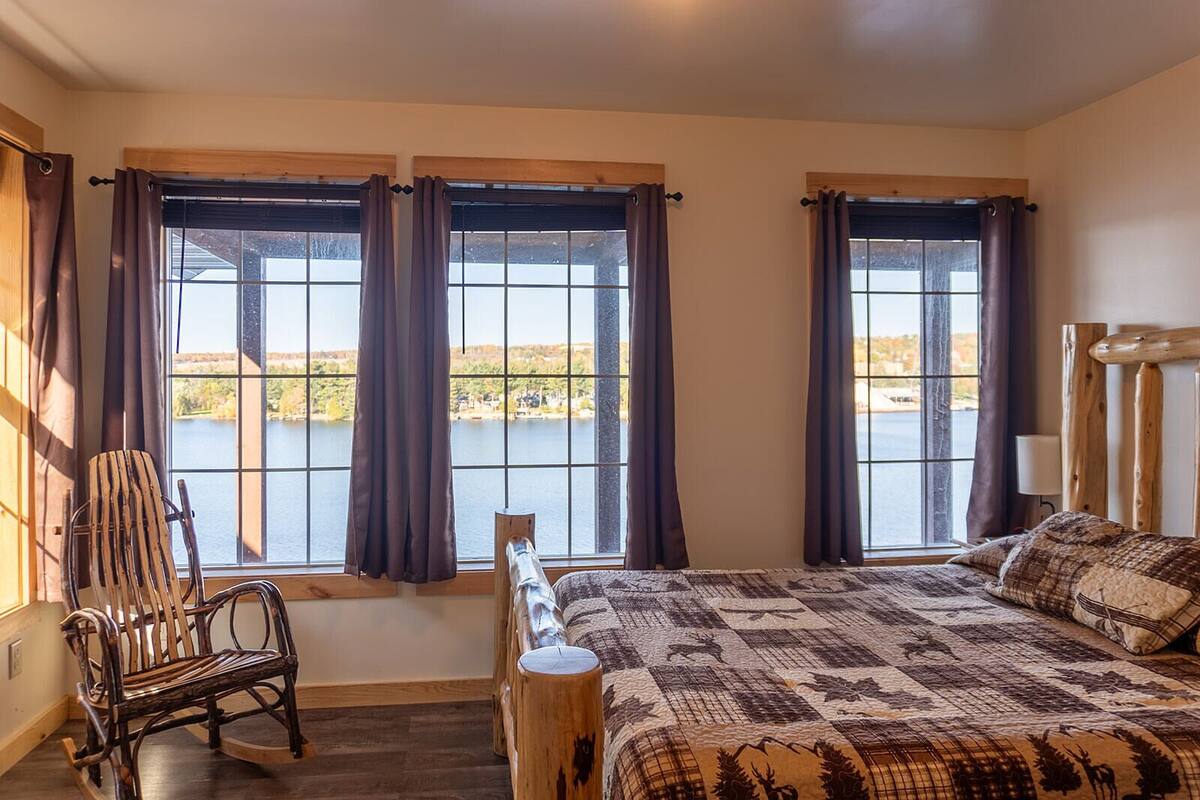 Een slaapkamer met een groot bed, een stoel en uitzicht op een meer door de ramen.