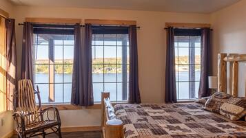 Une chambre avec un grand lit, une chaise et une vue sur un lac, visible à travers les fenêtres.