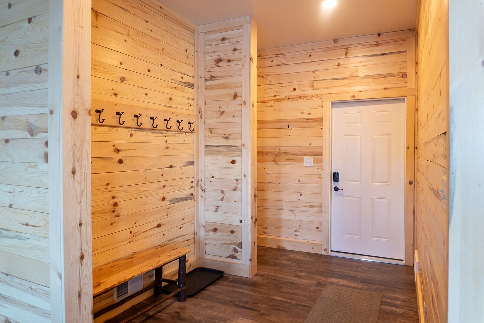 Un couloir intérieur en bois, avec un banc, une porte et un porte-manteau fixé au mur.
