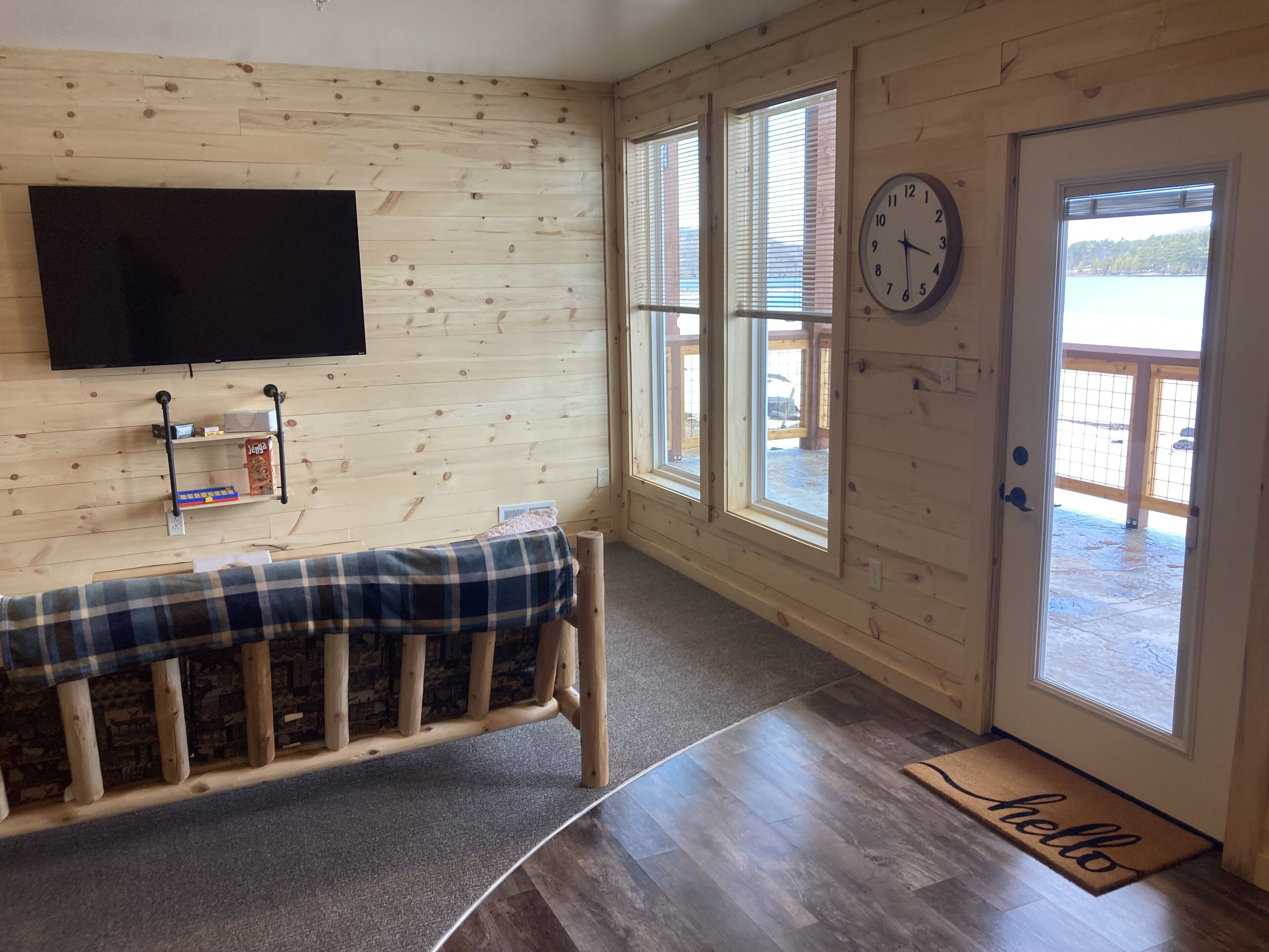 A room with wooden walls, a bench, a mounted clock, and a door leading outside.
