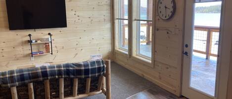 A room with wooden walls, a bench, a mounted clock, and a door leading outside.