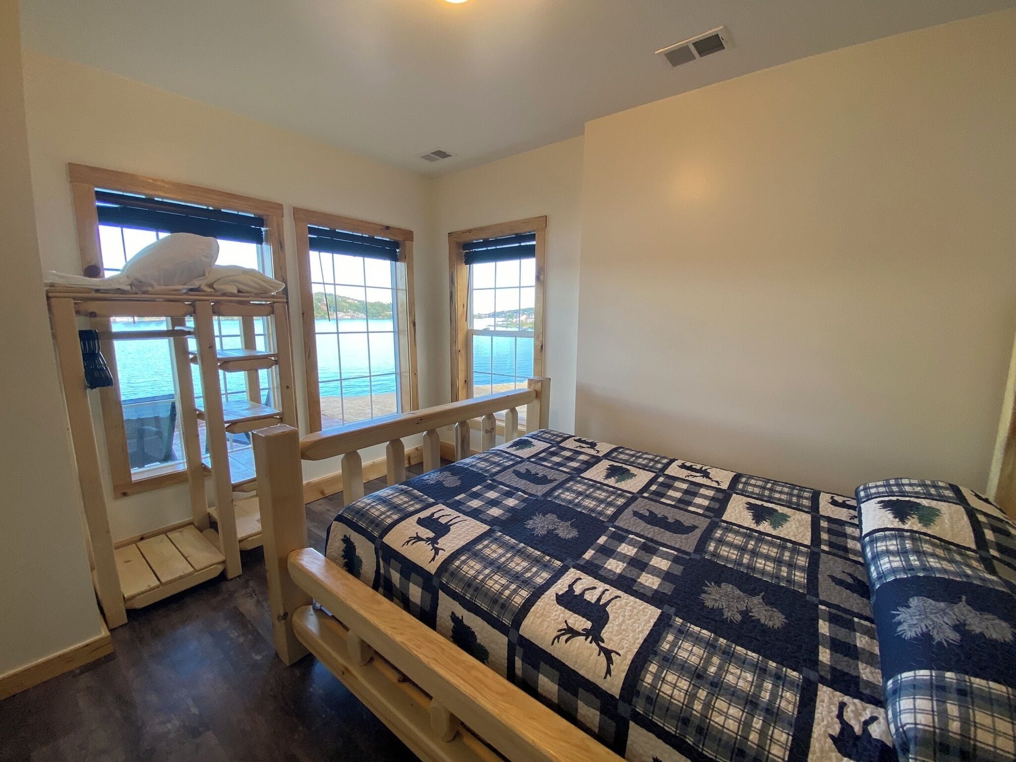A bedroom with a bunk bed, large windows with a view of the sea, and a checkered bedspread.