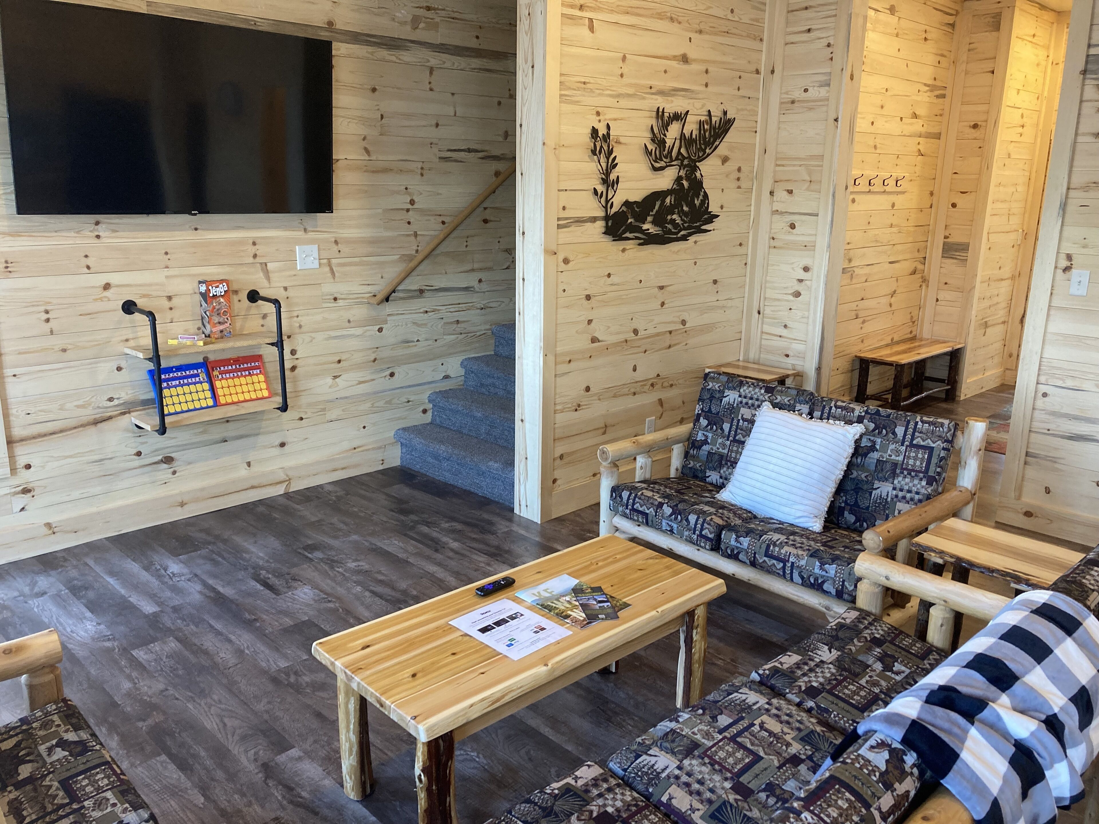 Interior acogedor de una cabaña con paredes de madera, un sofá, una mesa de centro y un televisor montado en la pared.