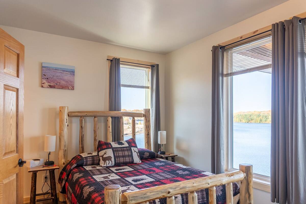 Een slaapkamer met een houten bed, uitzicht op een meer en een schilderij aan de muur.