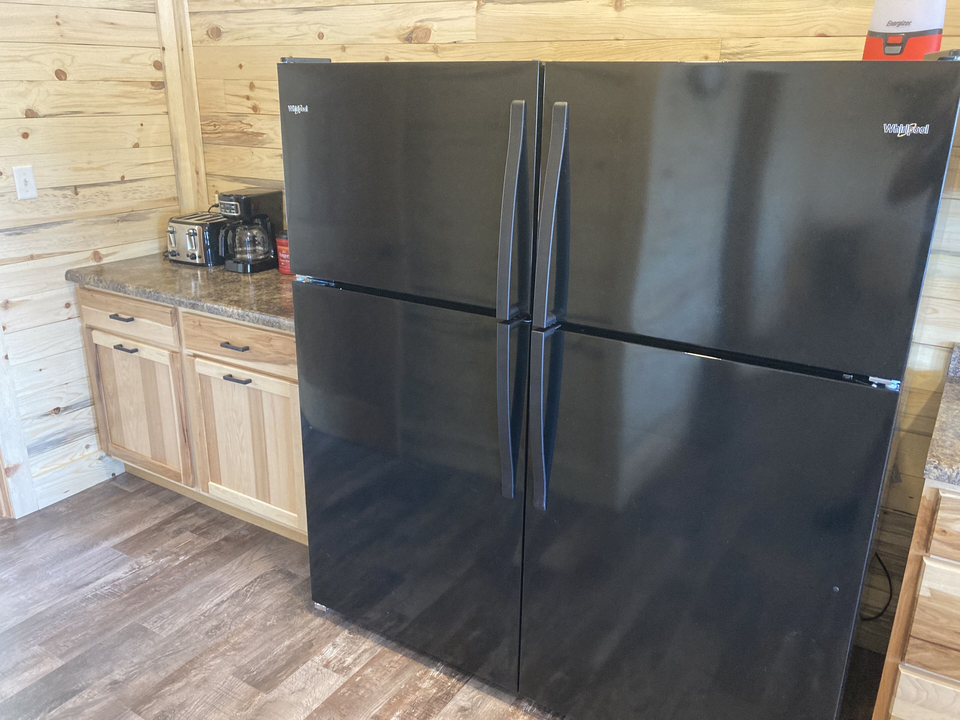 Un refrigerador Whirlpool negro en una cocina con armarios de madera y encimera de granito.