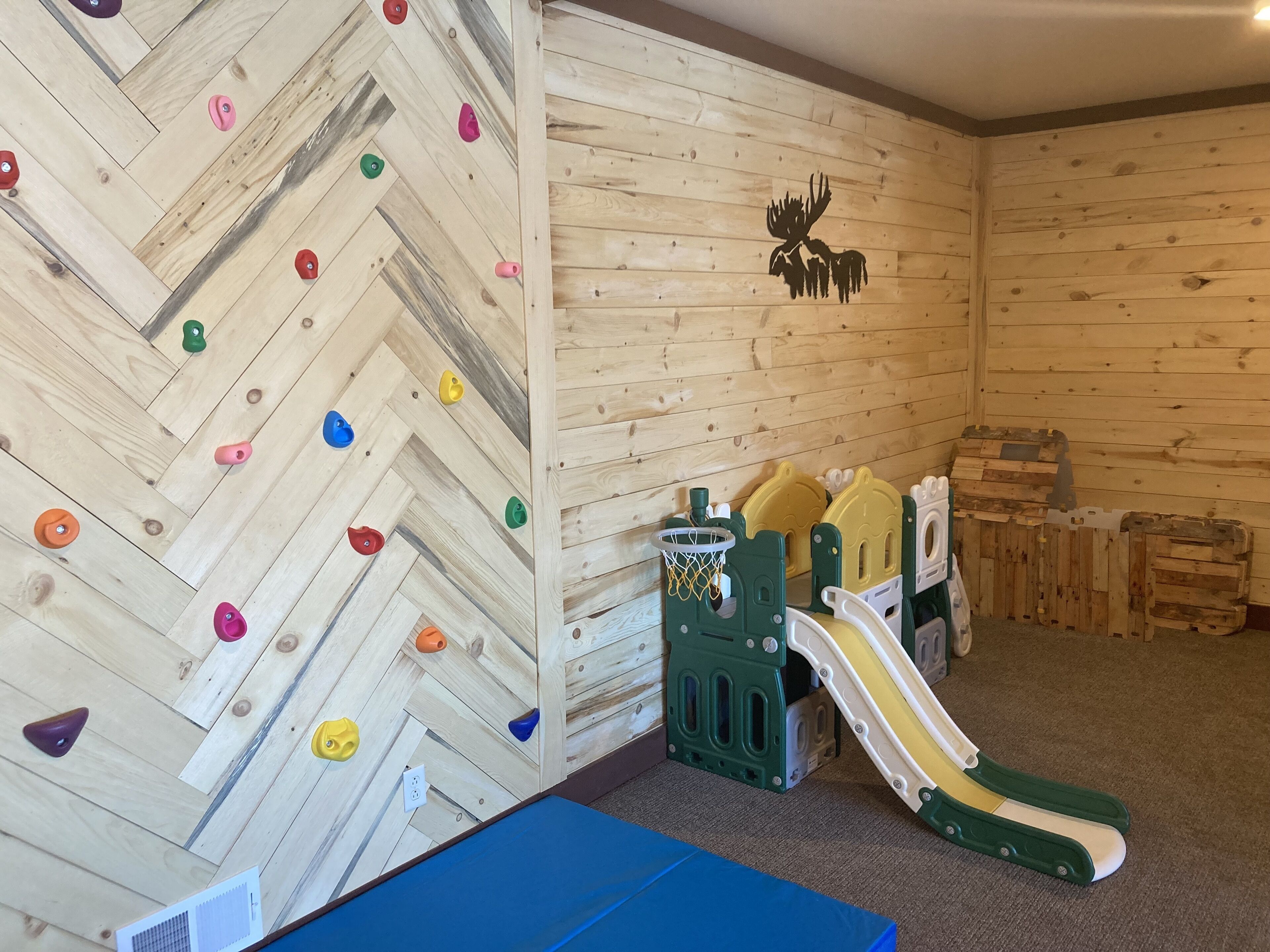 A climbing wall with colorful holds and a wooden wall with a moose silhouette.