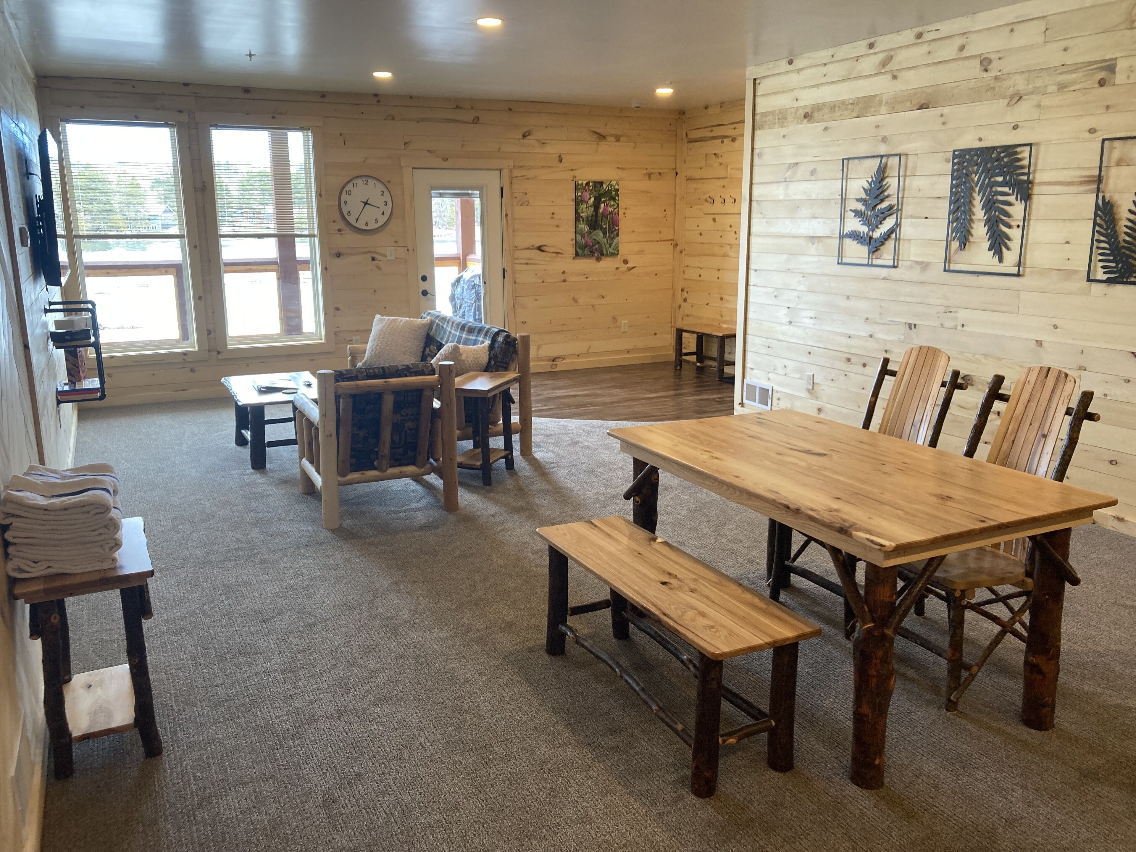 A cozy cabin interior with a wooden dining table, benches, a sofa, and a clock on the wall.