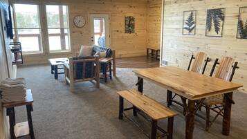 A cozy cabin interior with a wooden dining table, benches, a sofa, and a clock on the wall.