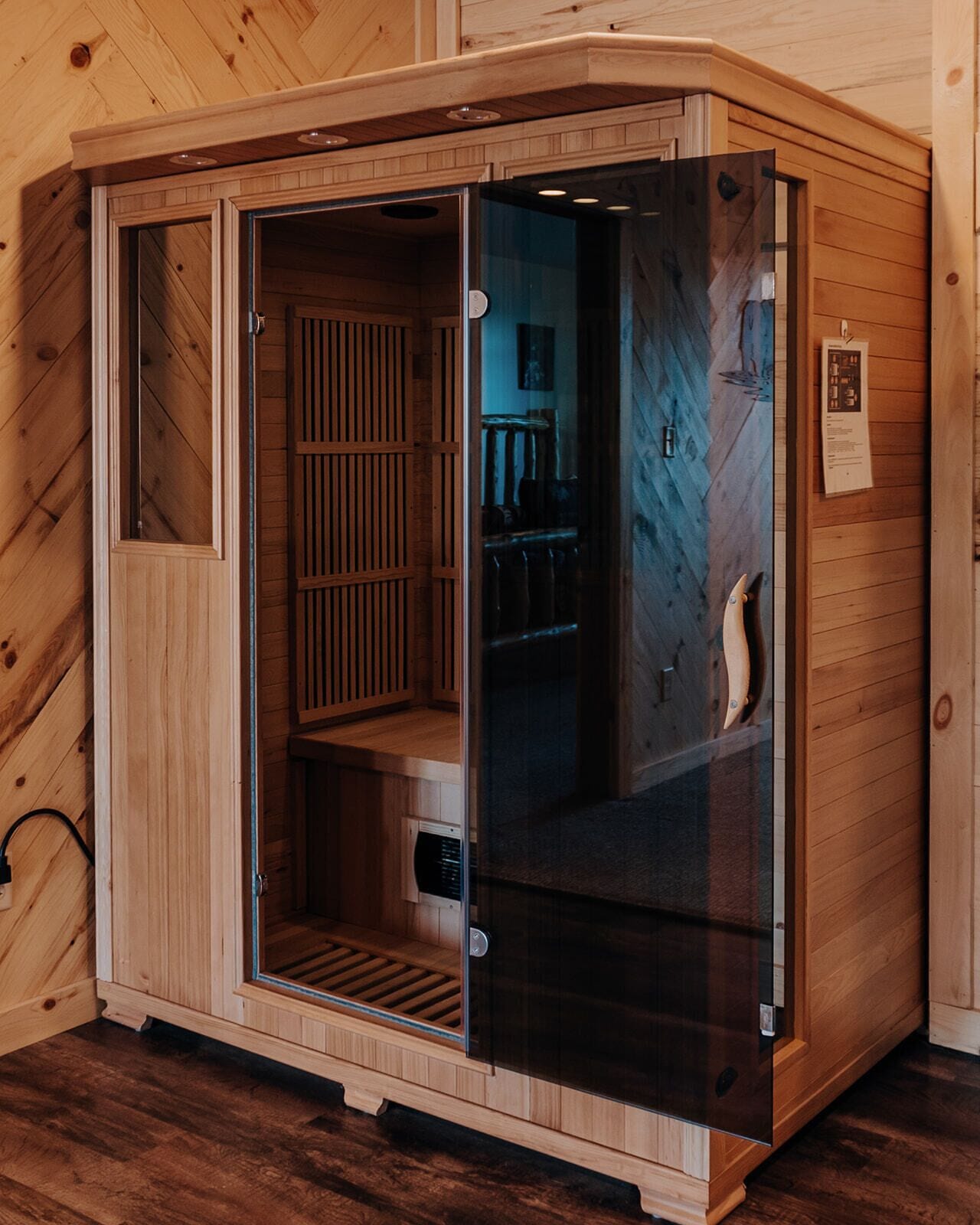 A wooden sauna with a glass door, a bench inside, and a small window.