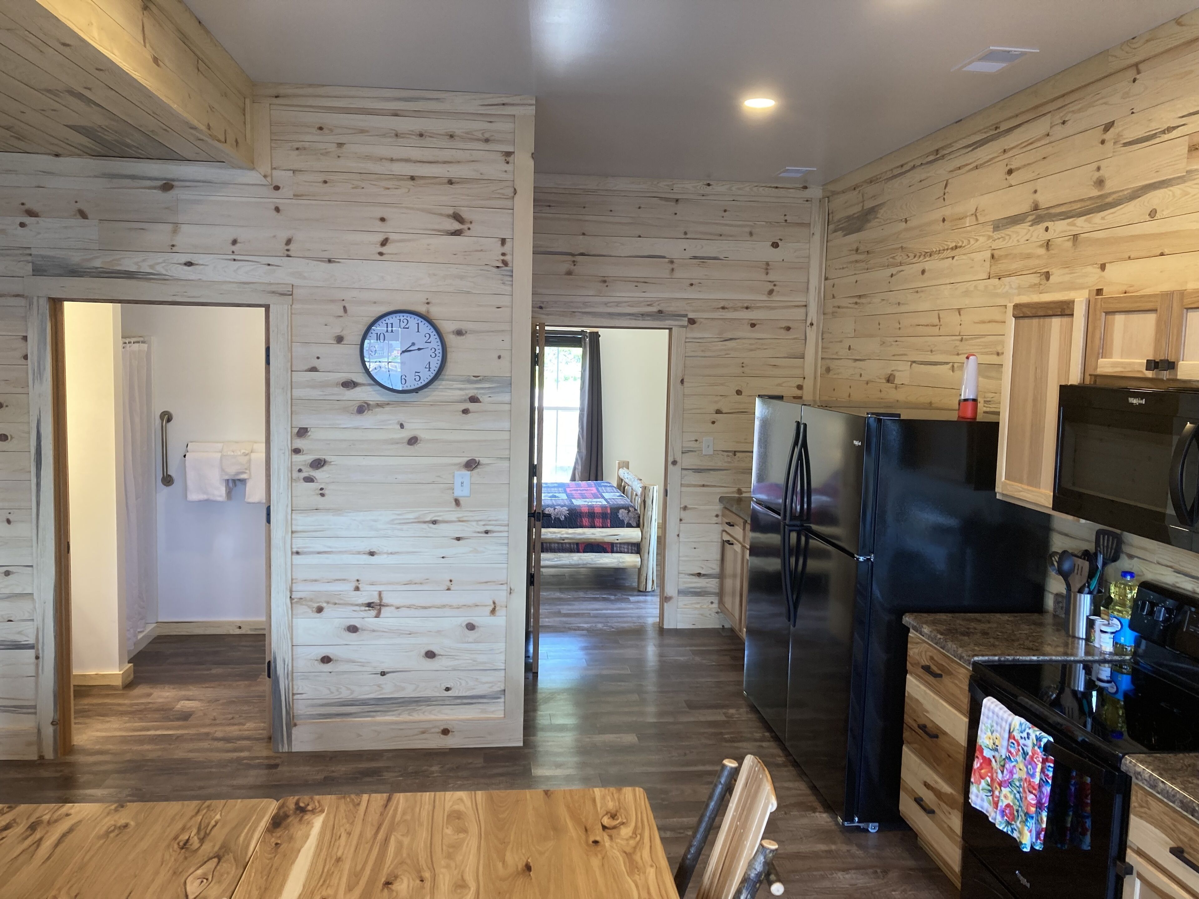 A modern kitchen with wooden paneling, a stainless steel refrigerator, and a dining area with a wooden table and chairs.