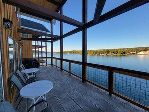 Um deck coberto com mesa e cadeiras, com vista para um lago e uma costa distante.
