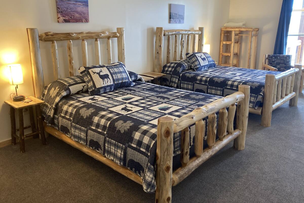Een kamer met twee houten bedden, elk met een ruitendekbed met dierenprint. Er staan nachtkastjes met lampen, en er hangt een schilderij aan de muur.