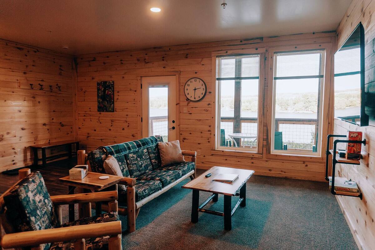 Een gezellige kamer in chaletstijl met houten inrichting, een bank, een bijzettafeltje en een klok aan de muur.