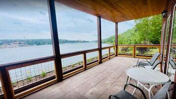 A covered outdoor area with a view of a river and hills. There are chairs and a table.