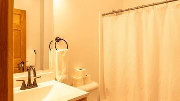 Un baño con lavamanos, espejo, toallero, papel higiénico y cortina de ducha.
