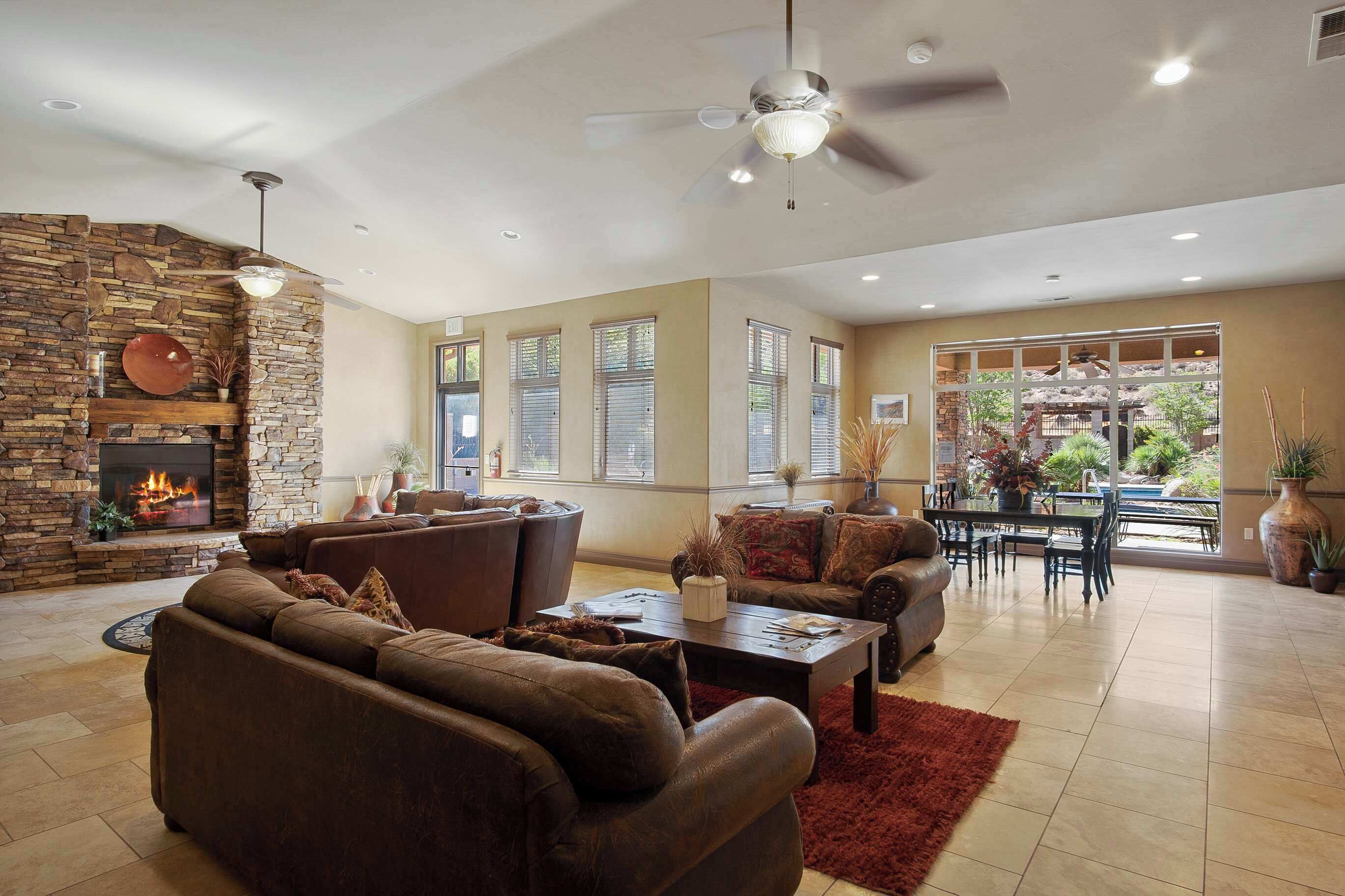 A spacious living room with a stone fireplace, leather sofas, a dining area, and large windows offering a view of the outdoors.