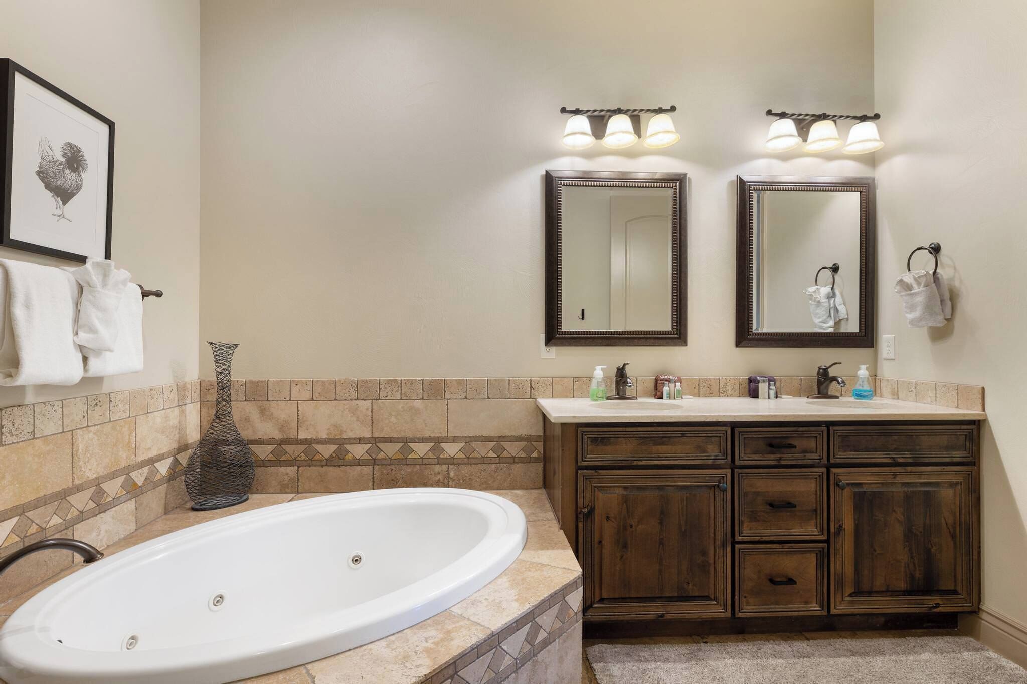 A bathroom with a large bathtub, two mirrors, a vanity with drawers, and a tiled backsplash.