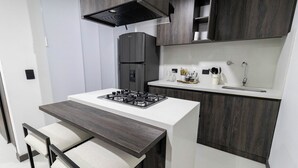 A modern kitchen with a central island, dark wood cabinetry, and a built-in gas stove. - Casa García Rent Home (Guatapé)