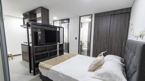 A modern bedroom with a bed, a TV, a wardrobe, and a bathroom visible through an open door. - Casa García Rent Home (Guatapé)