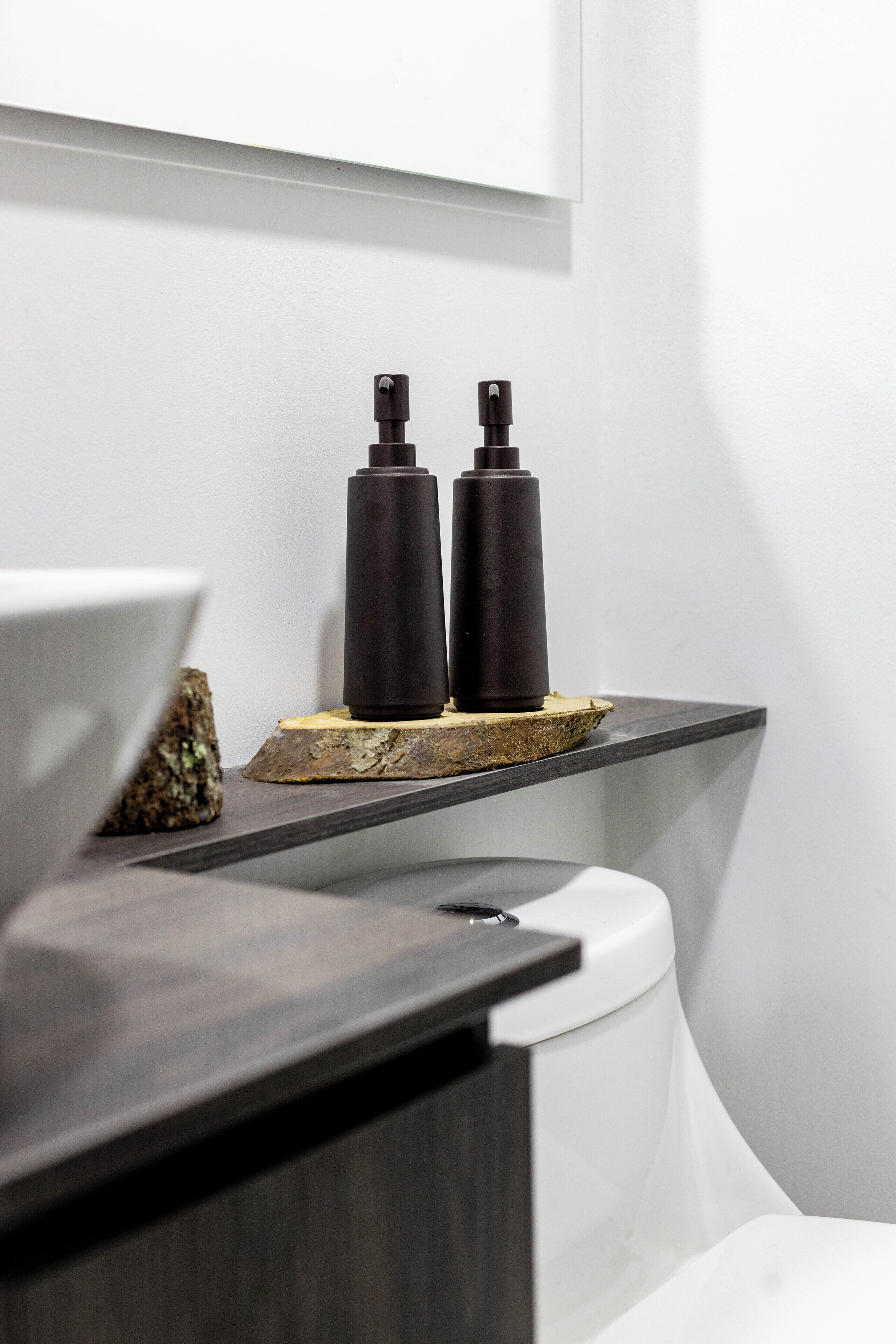 Ein modernes Badezimmer mit Toilette in Weiß, einem dunklen Holzwaschtisch und zwei schwarzen Flaschen auf einer Holzablage.
