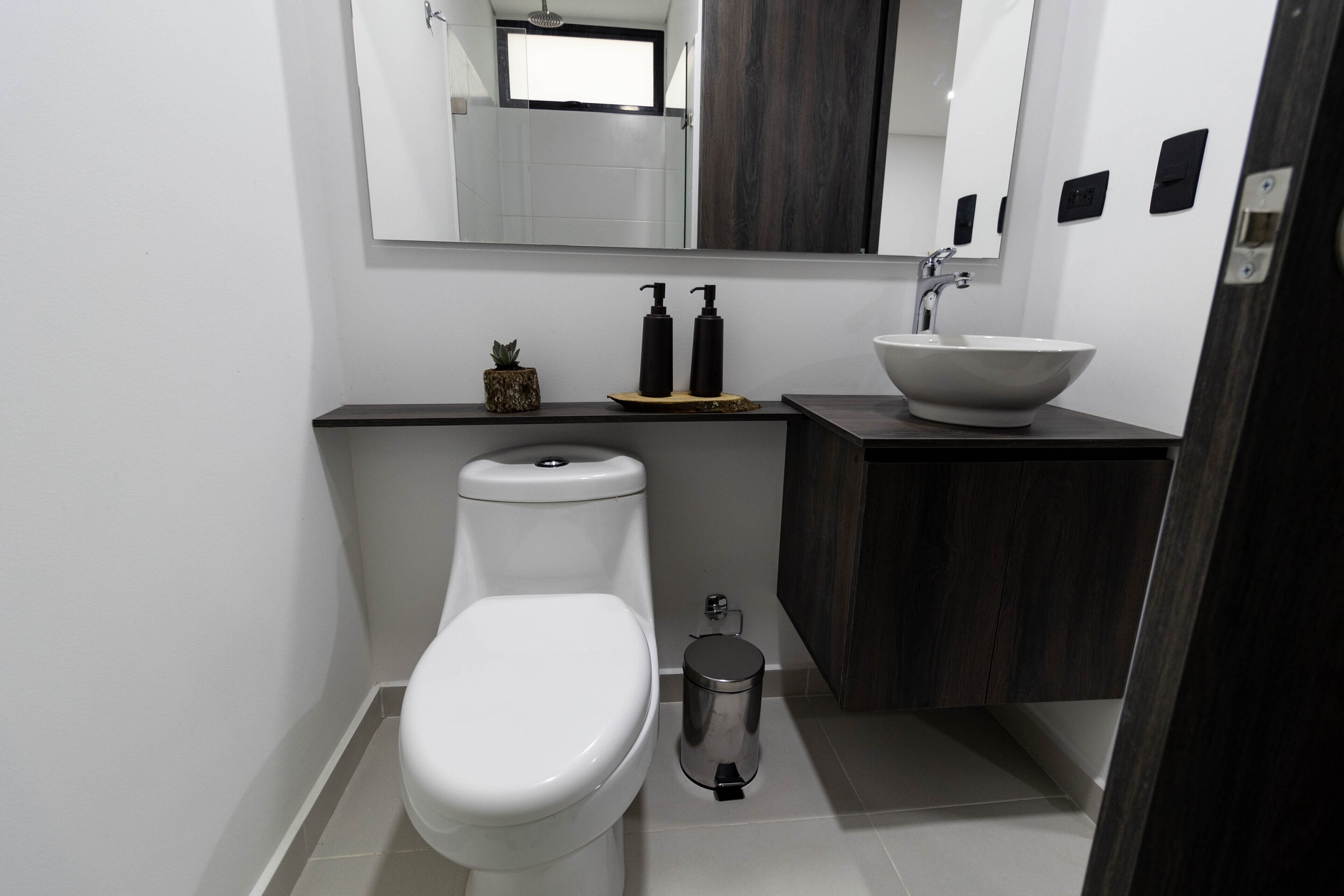 A modern bathroom with a white toilet, a sink with a vessel basin, and a mirror above.