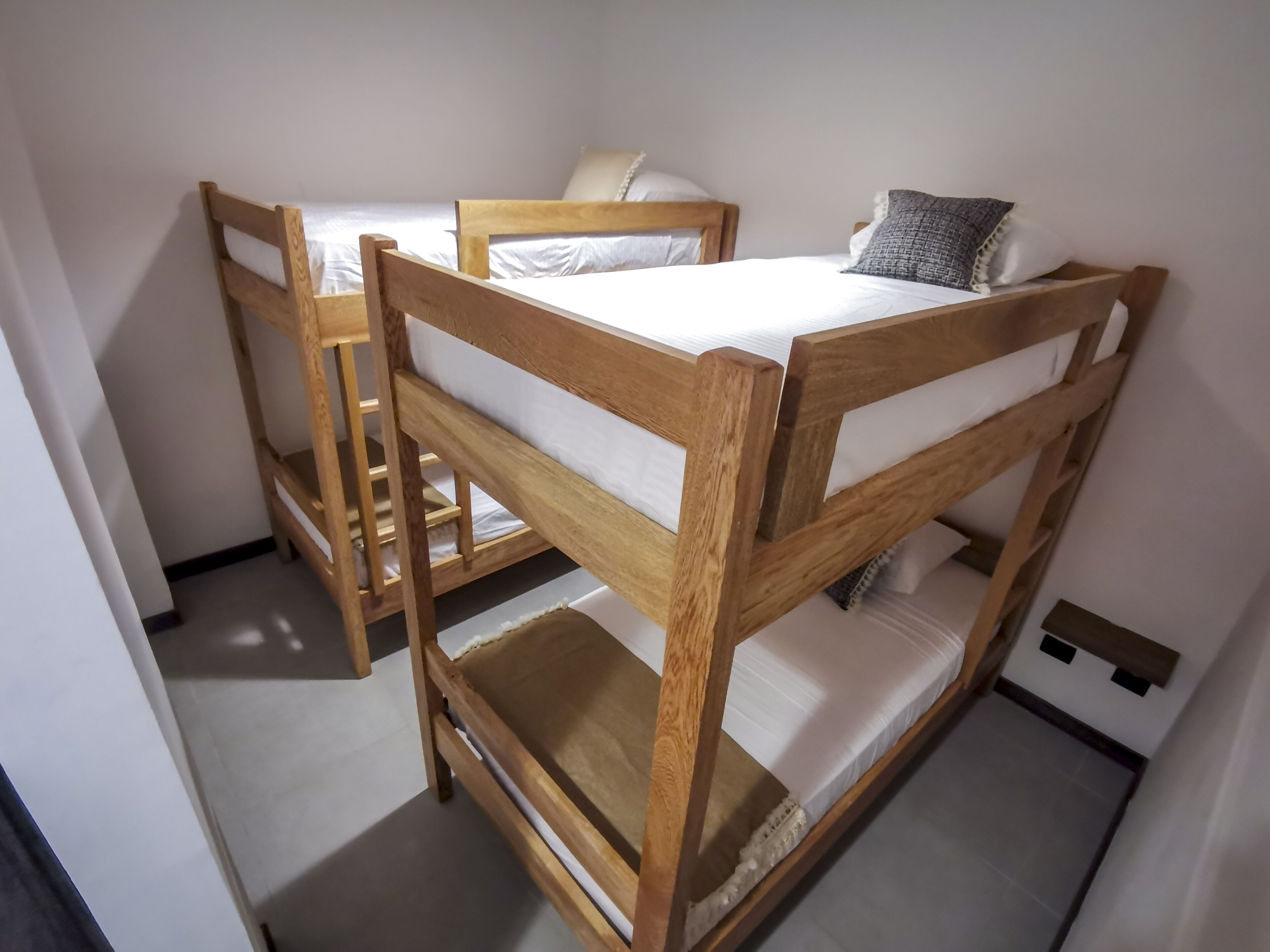 A room with two wooden bunk beds, each with a pillow and a blanket.