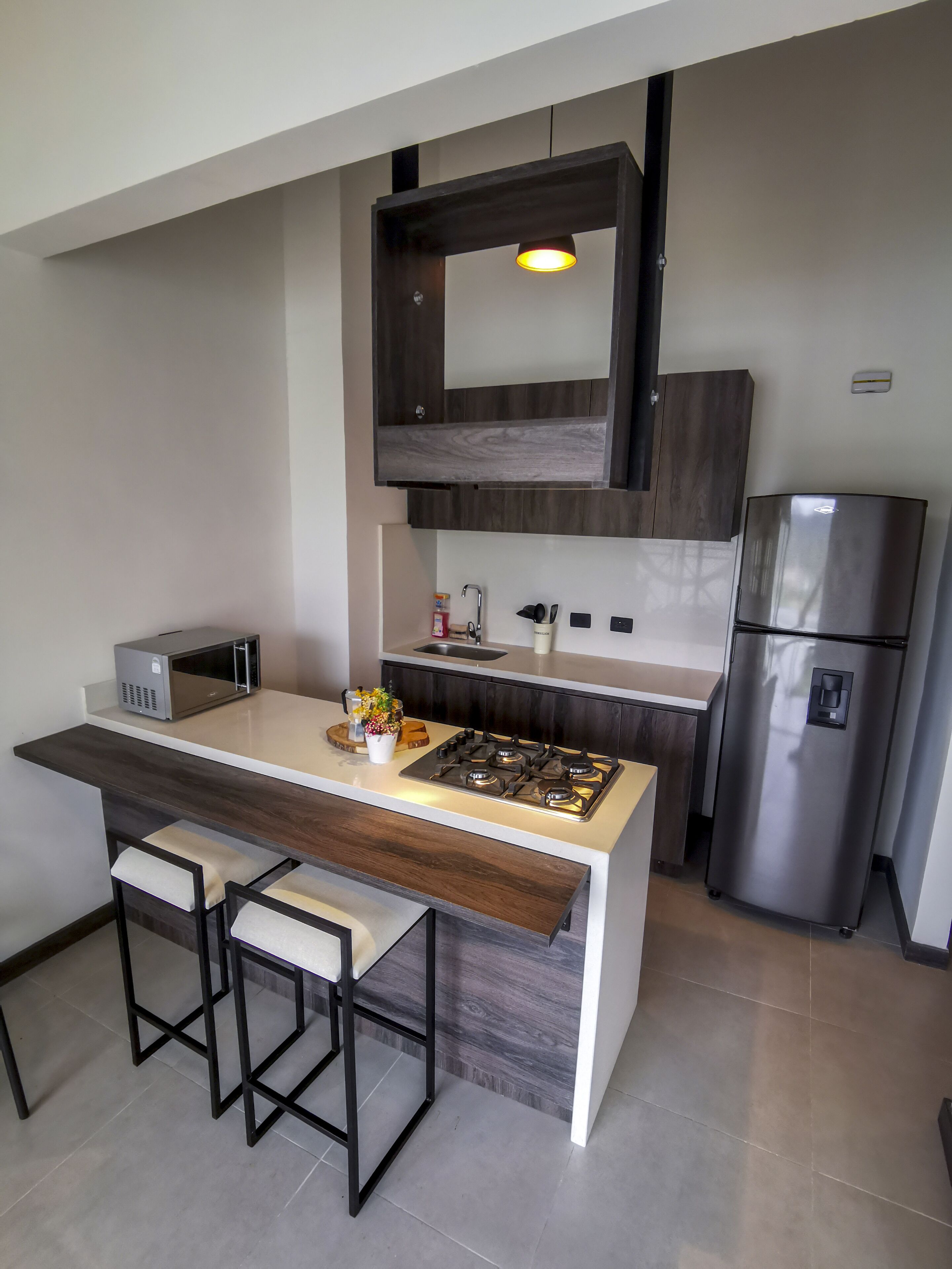 Een moderne keuken met een centraal eiland, barstoelen, een inbouwfornuis, een magnetron, een spoelbak en een koelkast.