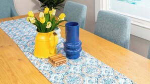 Un coin repas avec une table en bois, des chaises bleues, un vase jaune avec des fleurs et un vase bleu.