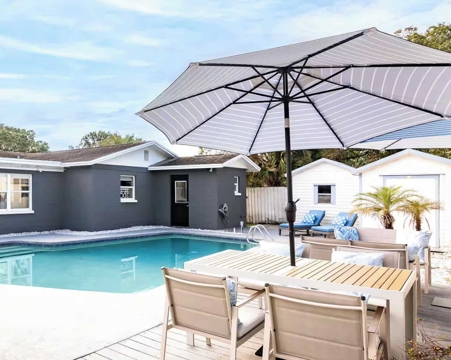 A swimming pool with a patio area, including a table and chairs, and a large umbrella.
