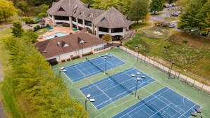 Un complejo de canchas de tenis con varias pistas, un edificio de diseño arquitectónico singular y zonas verdes circundantes.