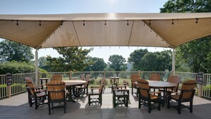Een terras buiten met tafels en stoelen, omringd door een witte hek en een grote luifel erboven.