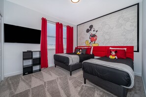 Ein Schlafzimmer mit zwei Betten, einem roten Vorhang, einem Wandbild mit Mickey Mouse und einem Fernseher an der Wand.