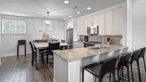 Una cocina moderna con encimeras de granito, electrodomésticos de acero inoxidable y una isla central con taburetes de bar.