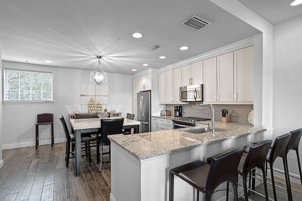 A modern kitchen with granite countertops, stainless steel appliances, and a central island with bar stools. - Seven Eagles Lavish: Water Park, Golf, Near Disney (Kissimmee)
