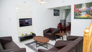 Una sala de estar moderna con un televisor de pantalla plana, sofás de cuero marrón, una mesa de centro de madera y un comedor con mesa y sillas de madera.