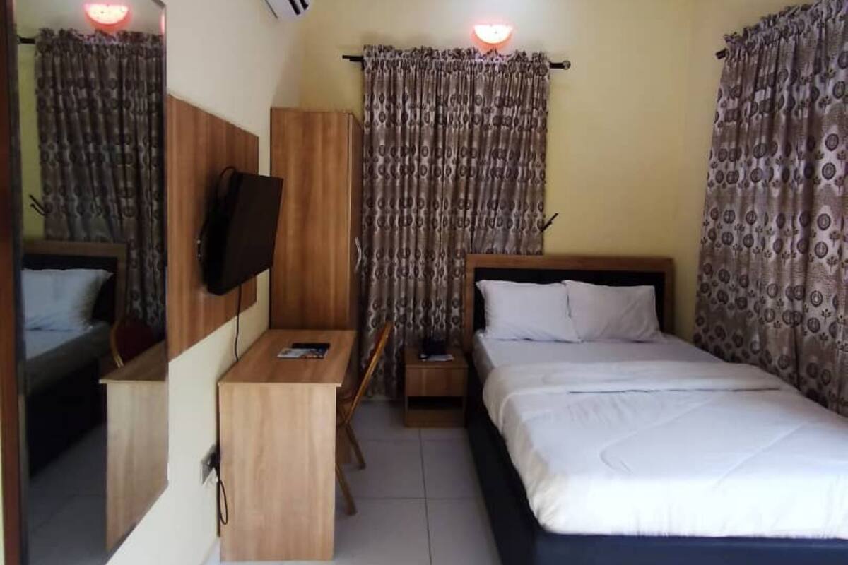 A hotel room with a bed, a desk, a TV, and curtains.