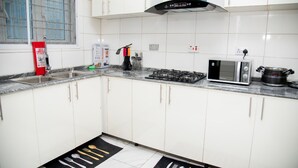 Una cocina con gabinetes blancos, estufa a gas, microondas y extintor.