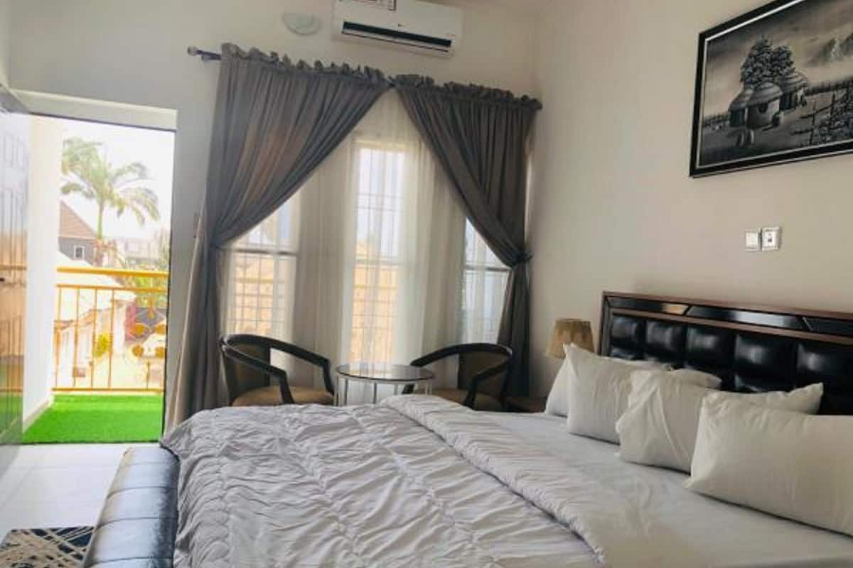 A hotel room with a large bed, two chairs, a small table, and a painting on the wall.