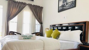 Una cama bien hecha con una colcha blanca y dos almohadas, cabecera de madera y un cuadro en la pared.