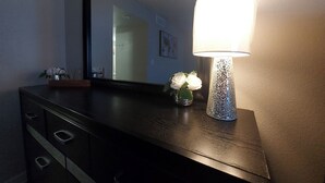 A dark wooden dresser with a mirror, a lit lamp, and a vase with white flowers. - Luxury Apt-- 1 mile from Strip (Las Vegas)