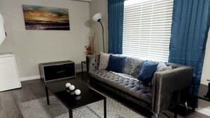A living room with a sofa, a coffee table with decorative balls, a painting on the wall, and a window with curtains. - Luxury Apt-- 1 mile from Strip (Las Vegas)